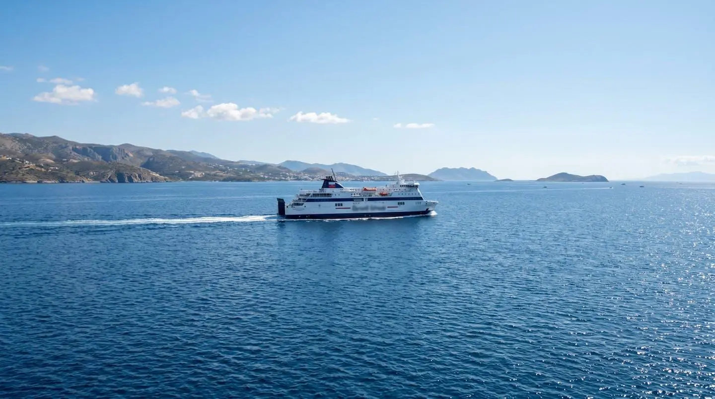 Ein modernes weisses Fährschiff mit blauen Akzenten gleitet durch das ruhige, tiefblaue Wasser des Mittelmeers unter klarem Himmel