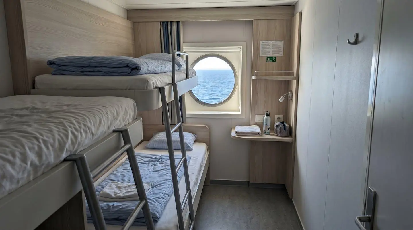 Moderne Innenkabine einer Fähre mit zwei Stockbetten, frischer weisser Bettwäsche und kleinem Fenster mit Meerblick